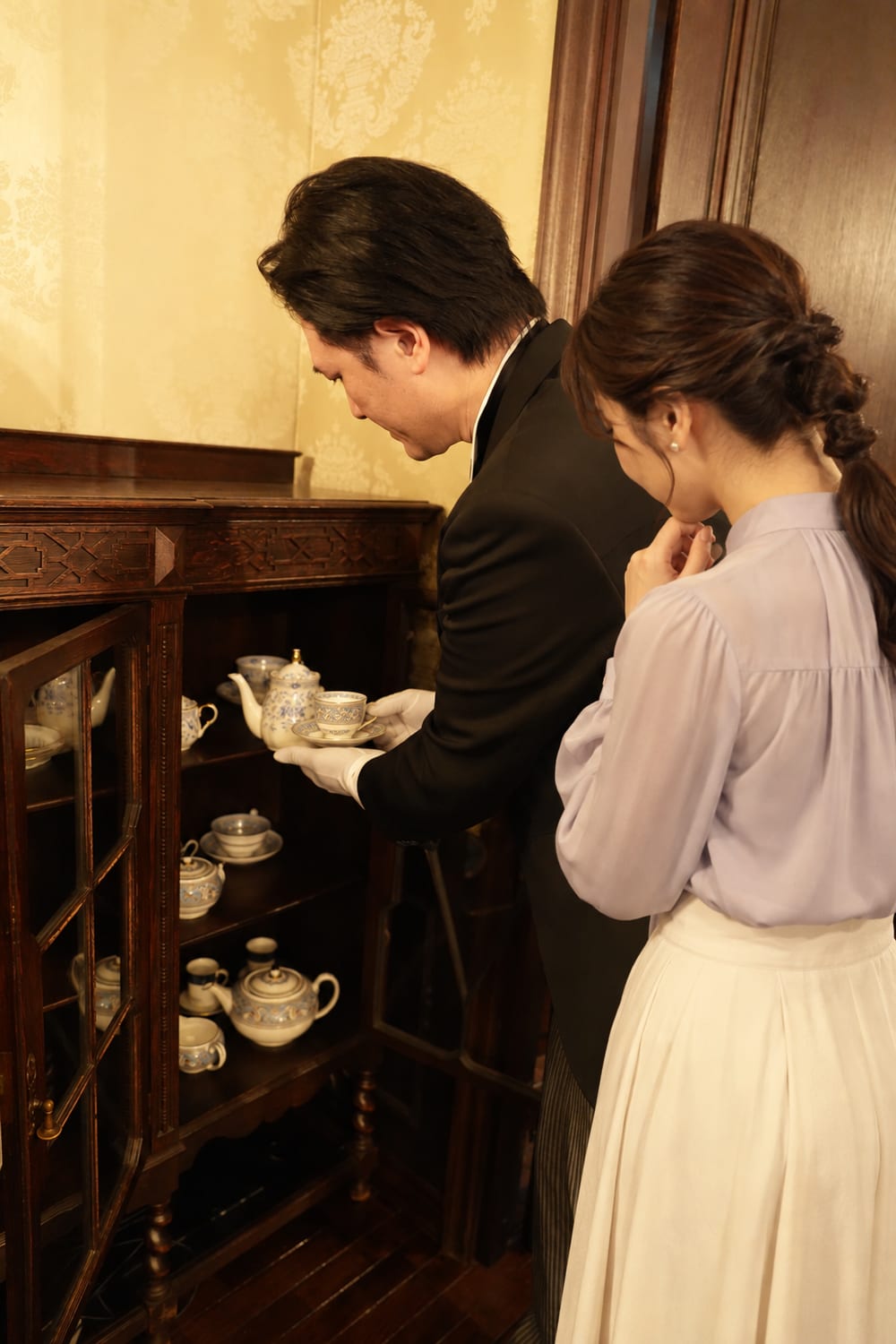 飾り棚の前で、茶器を選ぶご主人さまに付き添う執事